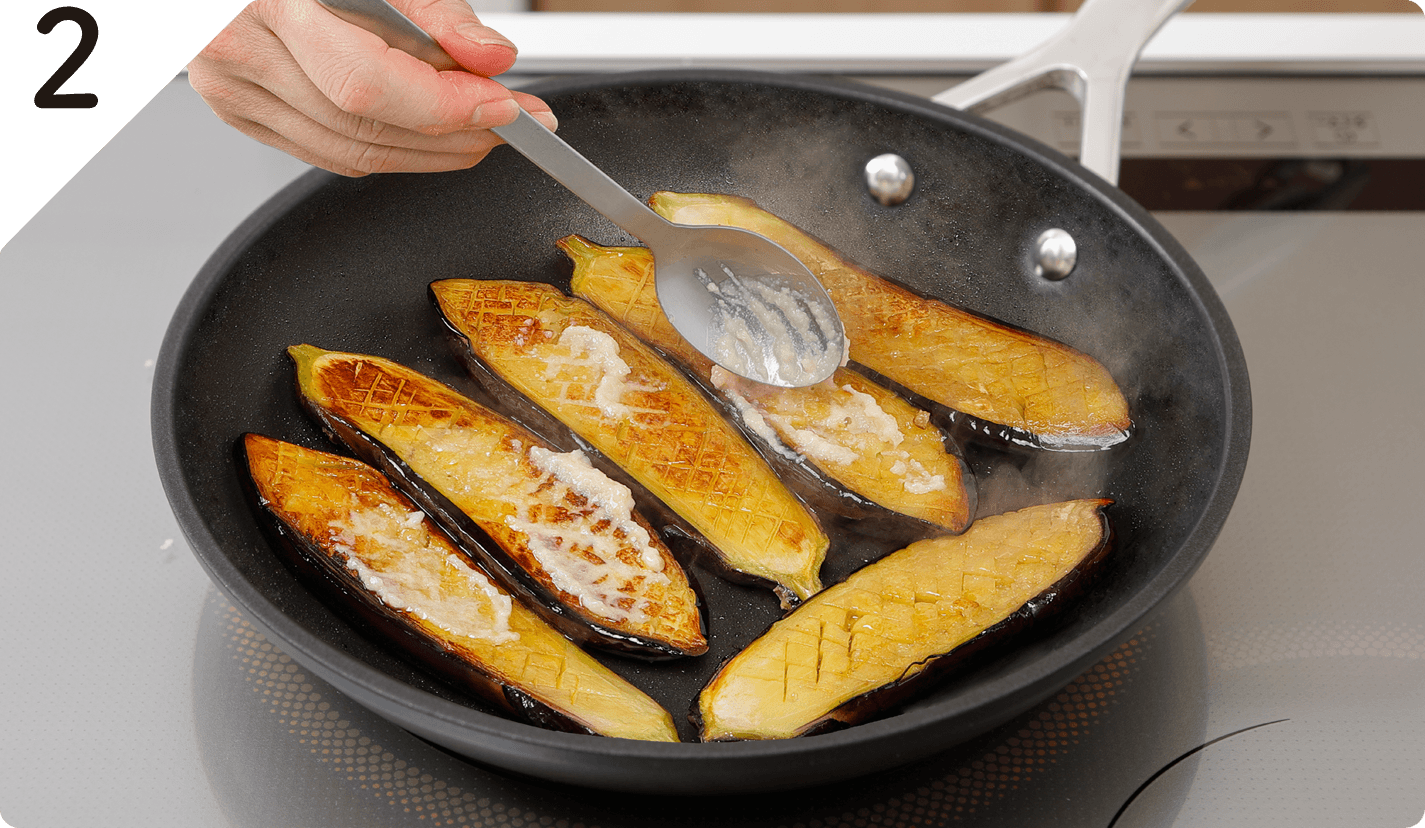 フライパンにオリーブオイルを中火で熱し、なすの切り口を下にして並べる。焼き色がついたら上下を返し、にんにくを表面に塗り、蓋をして約10分弱火で焼く。