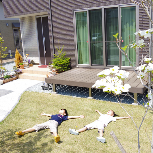 家の前の芝生で大の字になって対お湯の光を浴びている子どもと、満開になったハナミズキの写真