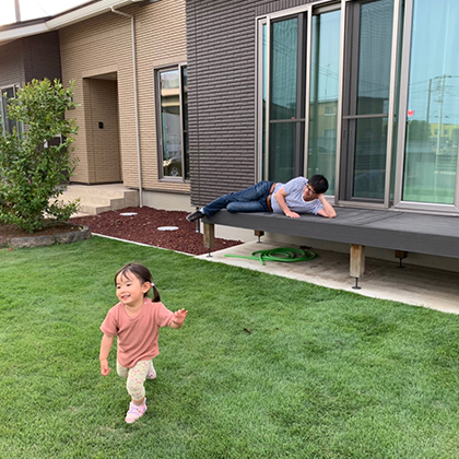 父がウッドデッキでゴロゴロしながら庭で走り回る娘を見守っています。