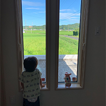 窓から田園風景を眺めている子どもの写真