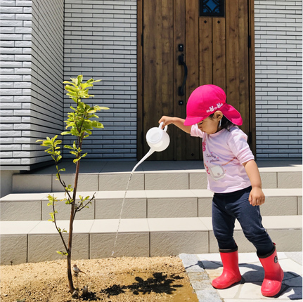 玄関の前の植物に水をあげている子どもの写真