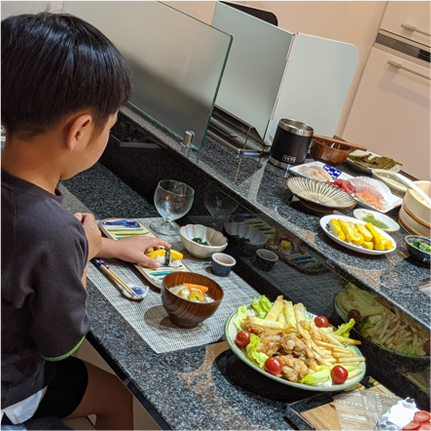 カウンターキッチンで寿司を握っている親とそれを食べている子どもの写真
