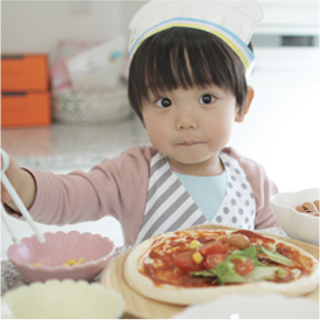 キッチンで帽子をかぶって料理を並べている子どもの写真