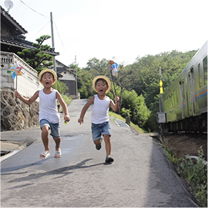 二人の子供が風車を持ちながら電車と競争している写真