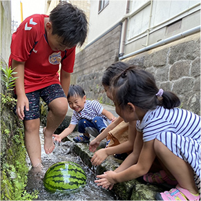 子どもたちが川でスイカを冷やしている写真