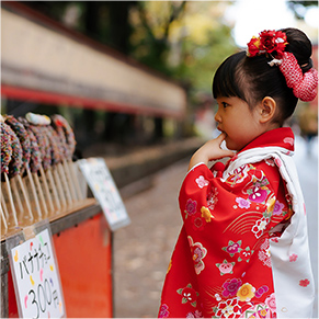 出店のバナナチョコを物欲しそうに見ている七五三の恰好をした子どもの写真