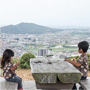 小山の上のベンチでパンを食べている子どもの写真