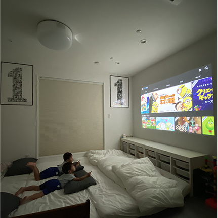 ベッドの上で壁に投影されたプロジェクターの映画を見ている子どもの写真