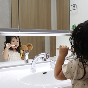 洗面台のキッズミラーでくまのぬいぐるみを持ちながら歯磨きをしている子どもの写真