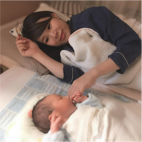寝ている赤ちゃんと横で微笑んでいる母親の写真